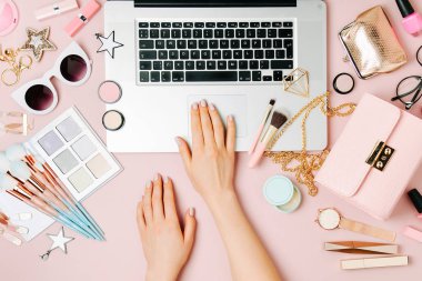 Moda blogger laptop ile çalışma. Kadın Aksesuar, kozmetik ürünleri soluk pembe tablo ile çalışma alanı. düz yatıyordu, en iyi görünümü