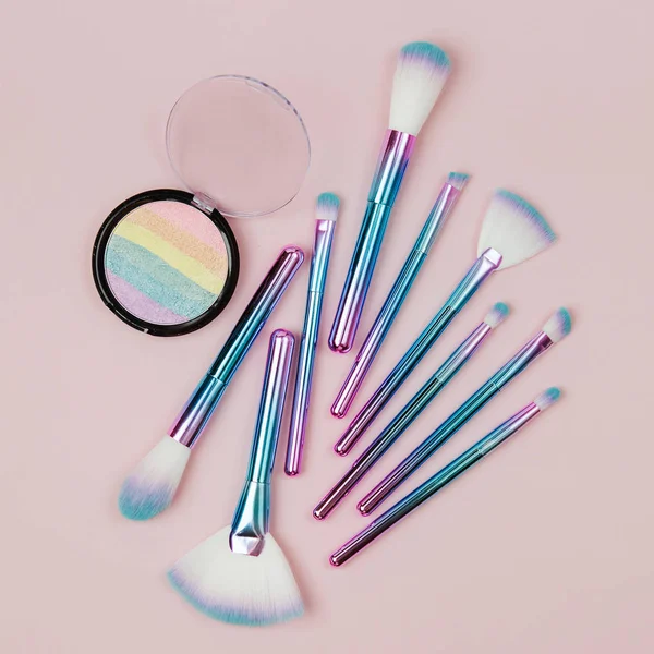 Fashion holographic colored makeup brushes with eye shadow and powder  on a pastel pink background. Flat lay, top view