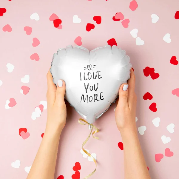 Female hands hold Balloon of heart shaped foil on pastel pink background. Love concept. Holiday celebration. Valentine\'s Day or wedding/bachelorette party decoration. Metallic balloon