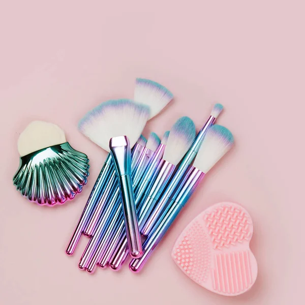 Fashion holographic colored makeup brushes with Brush Cleansing Pad on a pastel pink background. Flat lay, top view