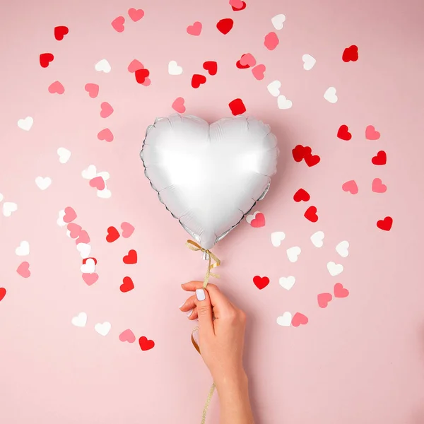 Female hands hold Balloon of heart shaped foil on pastel pink background. Love concept. Holiday celebration. Valentine\'s Day or wedding/bachelorette party decoration. Metallic balloon