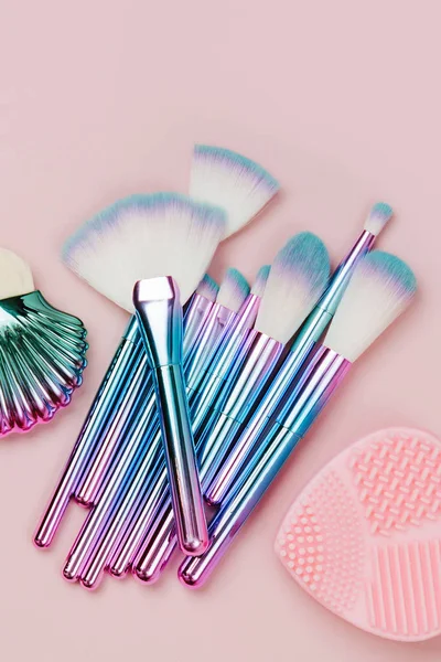 Fashion holographic colored makeup brushes with Brush Cleansing Pad on a pastel pink background. Flat lay, top view