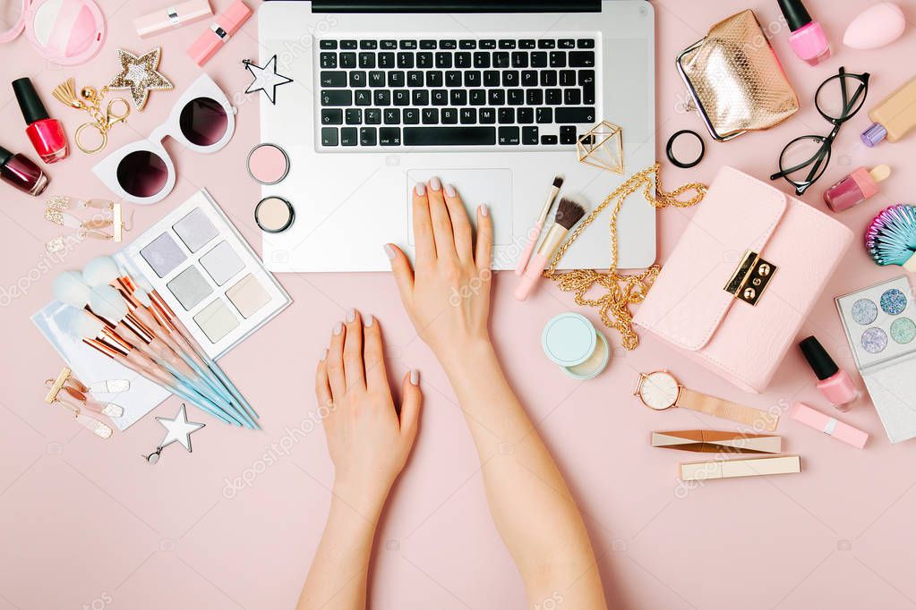 Fashion blogger working with laptop. Workspace with  female accessory, cosmetics products on pale pink table. flat lay, top view