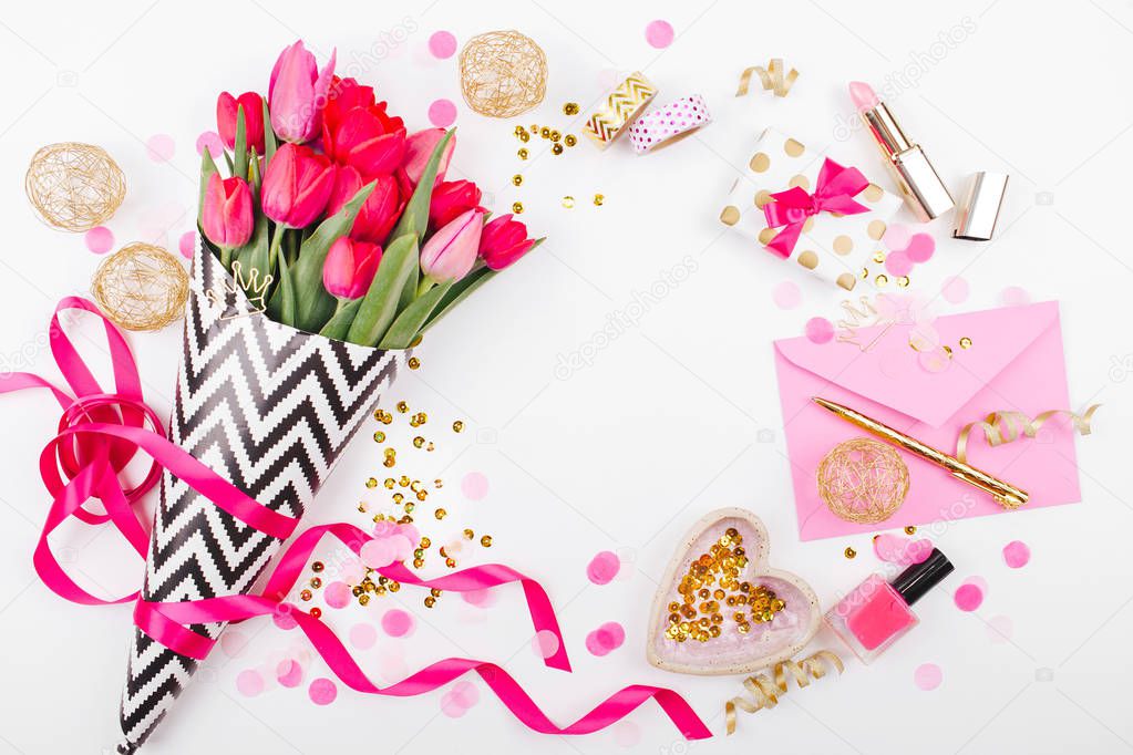 Pink and Gold Styled Desk with Florals. Pink tulips in black and white stylish wrapping paper, gifts, cosmetics and female accessories with confetti on white background