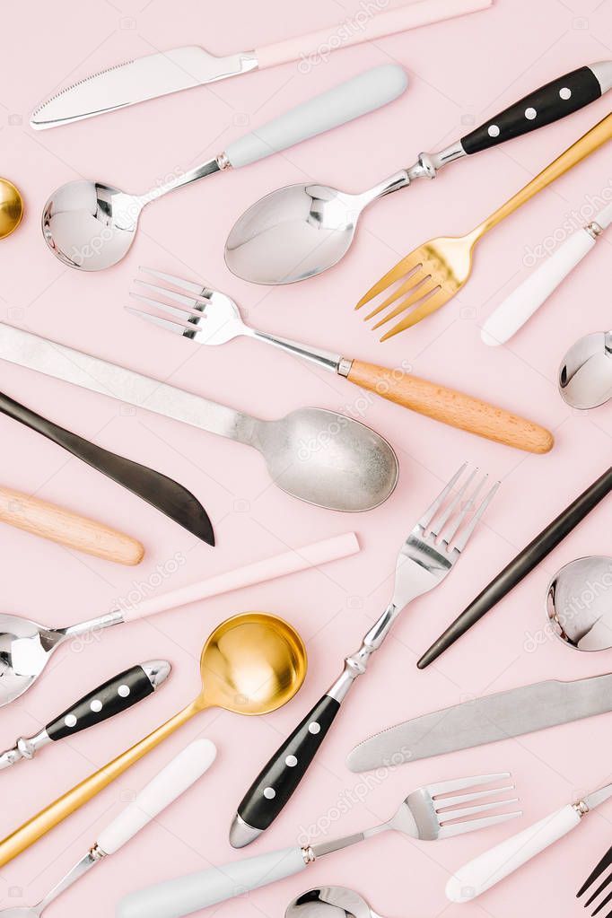 Spoons, forks and knives on light pink background