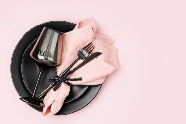 Çatal bıçak takımı, soluk pembe peçete, siyah plakalar ve pastel arka plan üzerinde şarap kadehi ile Festival tablo ayarı. Düz yatıyordu, en iyi görünümü