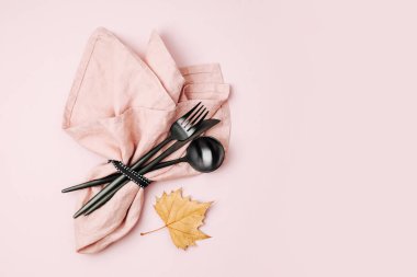 Siyah çatal bıçak takımı, soluk pembe peçete ve pastel arka plan üzerinde sonbahar yaprakları. Düz yatıyordu, en iyi görünümü