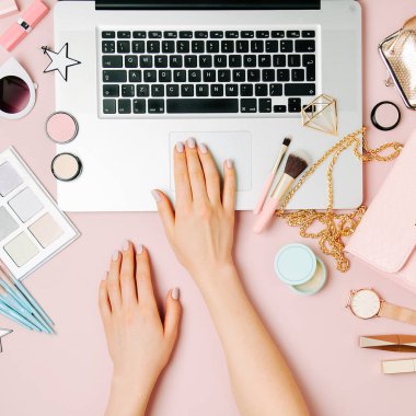 Moda blogger laptop ile çalışma. Kadın Aksesuar, kozmetik ürünleri soluk pembe tablo ile çalışma alanı. düz yatıyordu, en iyi görünümü