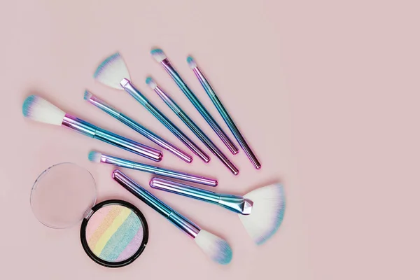 Fashion holographic colored makeup brushes with eye shadow and powder  on a pastel pink background. Flat lay, top view