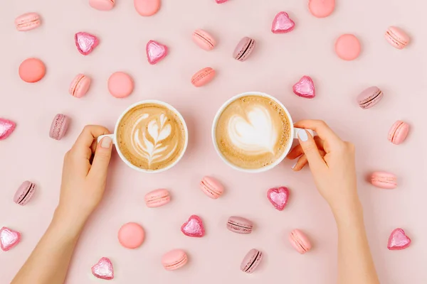 女性的手拿着卡布奇诺艺术的心脏形状在一个咖啡杯在浅粉色的背景 爱的概念 平面布局 顶部视图 — 图库照片