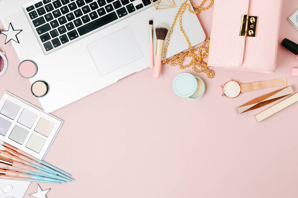 Fashion blogger workspace with laptop and female accessory, cosmetics products on pale pink table. flat lay, top view