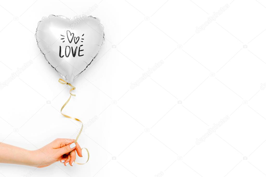 Female hands hold Balloon of heart shaped foil on white background. Love concept. Holiday celebration. Valentine's Day or wedding/bachelorette party decoration. Metallic balloon