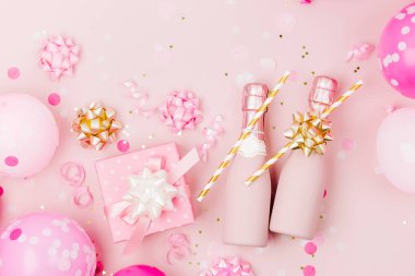 Mini şişe şampanya konfeti ve tinsel soluk pembe bir arka plan üzerinde