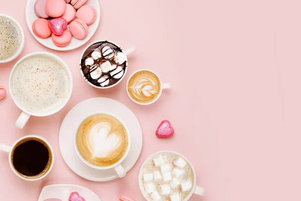 Various kinds of coffee in cups of different size with candys and macaroons on pale pink background