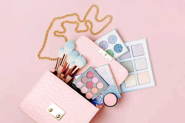 Cosmetic products flowing from Makeup bag on pastel pink background