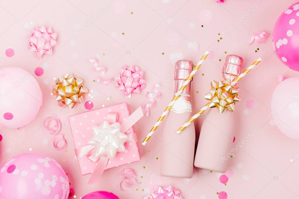 Mini bottles of champagne with confetti and tinsel on pale pink background