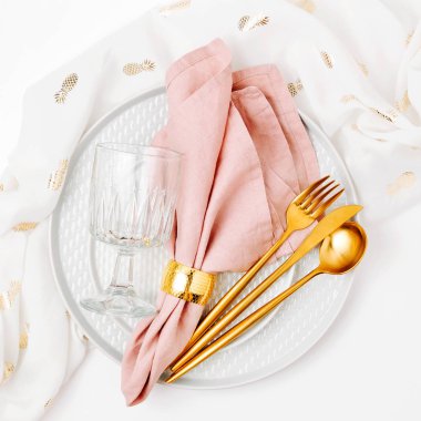 Kutlama masası. Beyaz arka planda pembe peçeteli tabak ve çatal bıçak takımı. Güzel düz yatak düzeni.