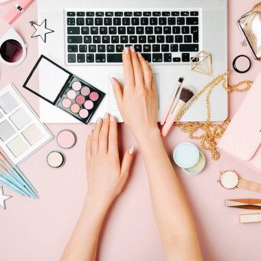 Moda blogger laptop ile çalışma. Kadın Aksesuar, kozmetik ürünleri soluk pembe tablo ile çalışma alanı. düz yatıyordu, en iyi görünümü