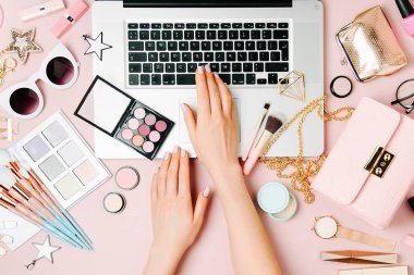 Moda blogger laptop ile çalışma. Kadın Aksesuar, kozmetik ürünleri soluk pembe tablo ile çalışma alanı. düz yatıyordu, en iyi görünümü