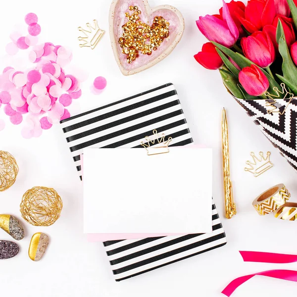 Pink and Gold Styled Desk with Florals. Pink tulips in black and white stylish wrapping paper, gifts, cosmetics and female accessories with confetti on white background