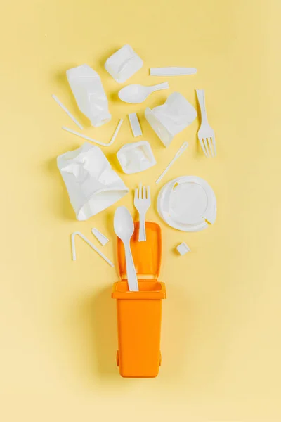 White single use plastic in garbage bin on  yellow background