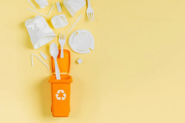 White single use plastic in garbage bin on  yellow background