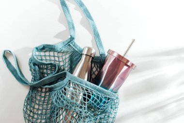 Yeniden kullanılabilir metal su şişesi ve beyaz arka plan üzerinde cup ile örgü çanta. Sürdürülebilir bir yaşam tarzı. Sıfır atık kavramı. Hiçbir plastik.