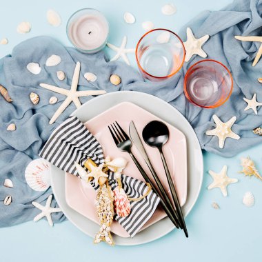 Sofra ve deniz süslemeleri şenlikli bir tablo hizmet için. Tabaklar, şarap, gözlük ve çatal bıçak takımı mavi zemin üzerine. Yaz konsepti. Düz yatıyordu, en iyi görünümü