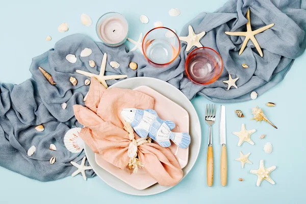 Tableware and sea decorations for serving a festive table. Plates, wine glasses and cutlery on blue background. Summer concept. Flat lay, top view