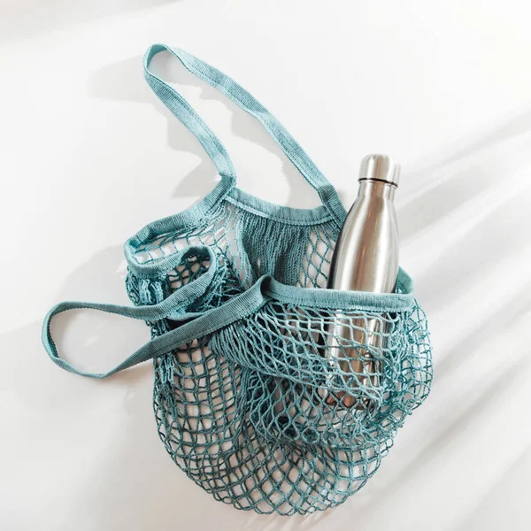 Mesh bags with reusable metal water bottle on white background. Sustainable lifestyle. Zero waste concept. No plastic.