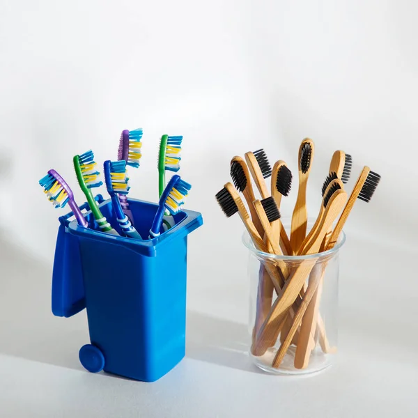 Eco friendly bamboo toothbrushes in glass and plastic toothbrushes in trash bin. Zero waste, plastic free, ecology concept.