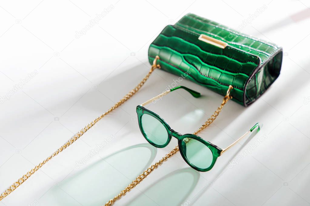Fashion green handbag with sunglasses on white background. Flat lay, top view. Summer fashion concept
