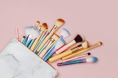 Bir pastel pembe arka plan üzerinde kozmetik çanta Moda çeşitli makyaj fırçaları. Düz döşeme, üst görünüm