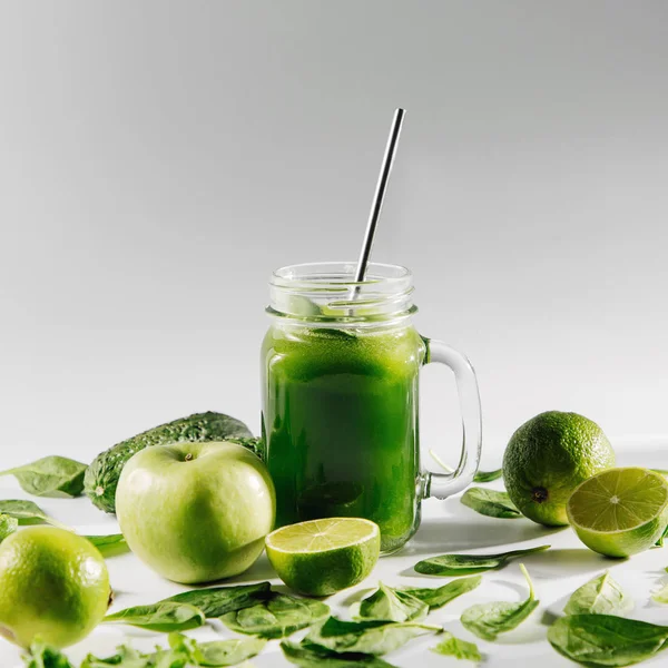 Healthy green smoothie with spinach and green fruits and vegetables on white table.