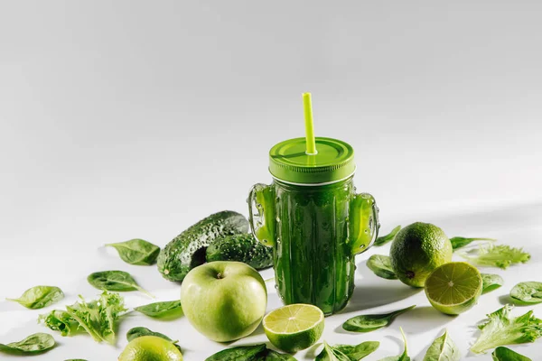 Green smoothie in cute glass jar shape of cactus with spinach and green fruits and vegetables on white table. Vegetarian food. Detox and diet concept.