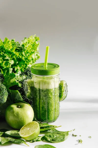 Green smoothie in cute glass jar shape of cactus with spinach and green fruits and vegetables on white table. Vegetarian food. Detox and diet concept.