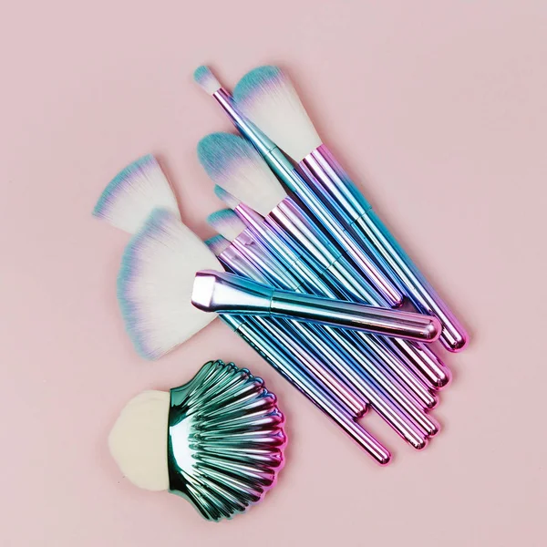 Fashion holographic colored makeup brushes on a pastel pink background. Flat lay, top view