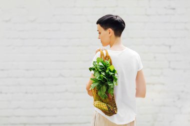 Hafif yaz kıyafetleri içinde, sebze ve yeşillik dolu bir çantayla genç bir kadın. Sürdürülebilir yaşam tarzı. Çevre dostu kavram.