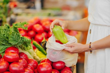 Kadın elleri meyve ve sebzeleri pamuğun içinde koyar ve gıda pazarında poşet üretir. Alışveriş için yeniden kullanılabilir eko çanta. Sıfır atık kavramı.