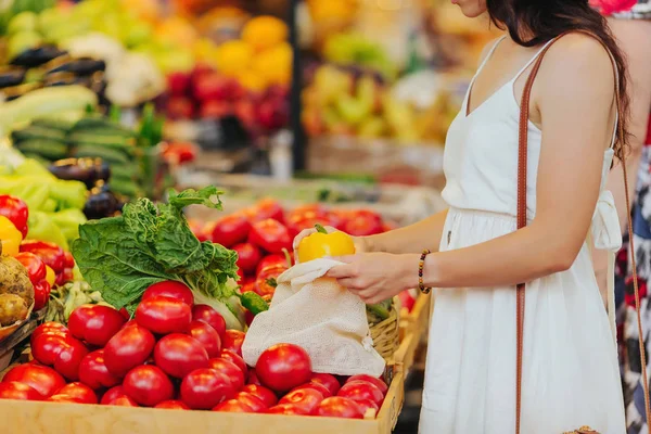 若い女性は 食品市場で綿の生産袋に果物や野菜を置きます 買い物に再利用可能なエコバッグ 廃棄物ゼロの概念 — ストック写真