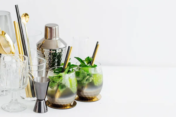 Cocktail with lime, mint and ice and bar accessories on white table