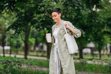 Kısa saçlı kadın yeniden kahve bardağı ve Eko Çanta sabah zevk tutarak. Çevre dostu konsept.