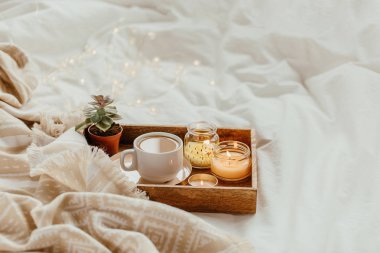 Beyaz yatak üzerinde sıcak ekose ile kahve ve mum tepsisi 