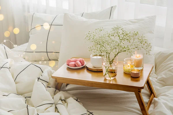 Wooden tray of coffee and candles with flowers on bed