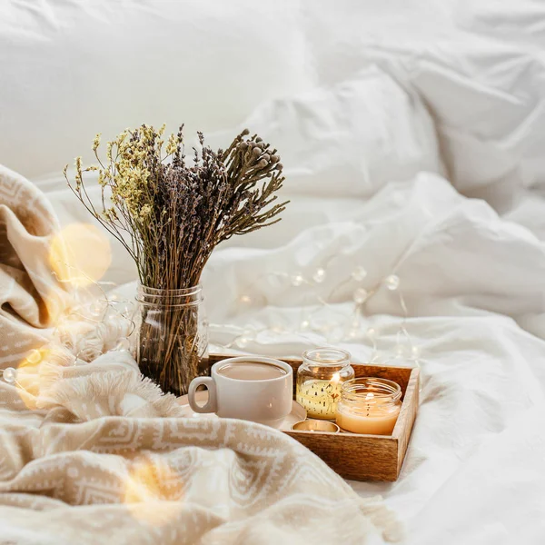Tray of coffee and candles with warm plaid on white bedding
