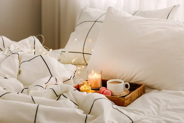 Wooden tray of coffee and candles on bed, hygge concept
