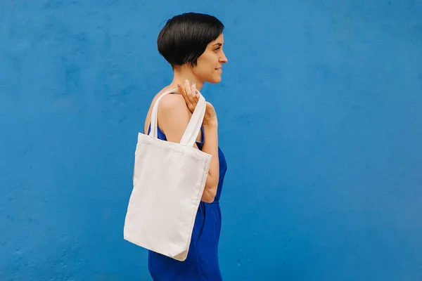 Woman holding canvas tote bag on bright blue background in the city. Reusable eco bag. Eco friendly concept.