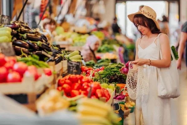 若い女性は 食品市場で綿の生産袋に果物や野菜を置きます 買い物に再利用可能なエコバッグ 廃棄物ゼロの概念 — ストック写真