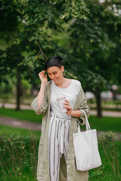 Kısa saçlı kadın yeniden kahve bardağı ve Eko Çanta sabah zevk tutarak. Çevre dostu konsept.