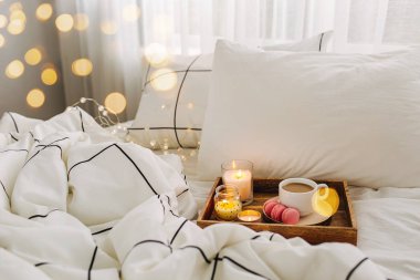 Yatakta ki tahta kahve tepsisi ve mumlar. Çizgili battaniye ve yastık ile beyaz yatak çarşafları. Yatakta kahvaltı. Hygge kavramı.